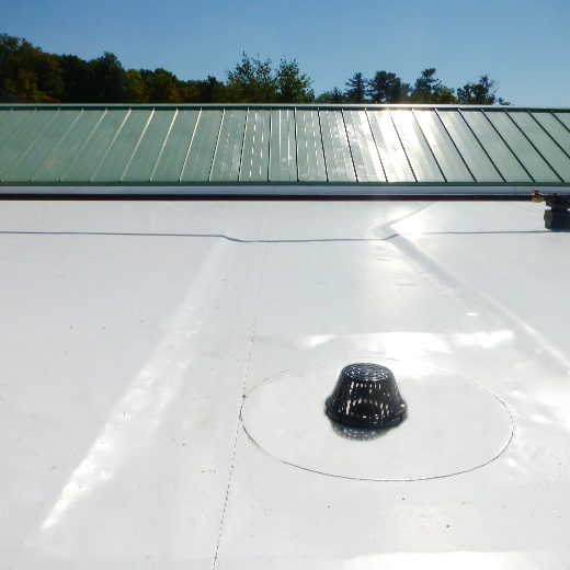 close up of flat roof leading to slanted, gray metal roof with trees and sky in the background