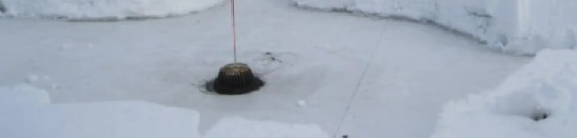 A roof drain with a pole sticking out.  Ice and snow are surrounding the drain.