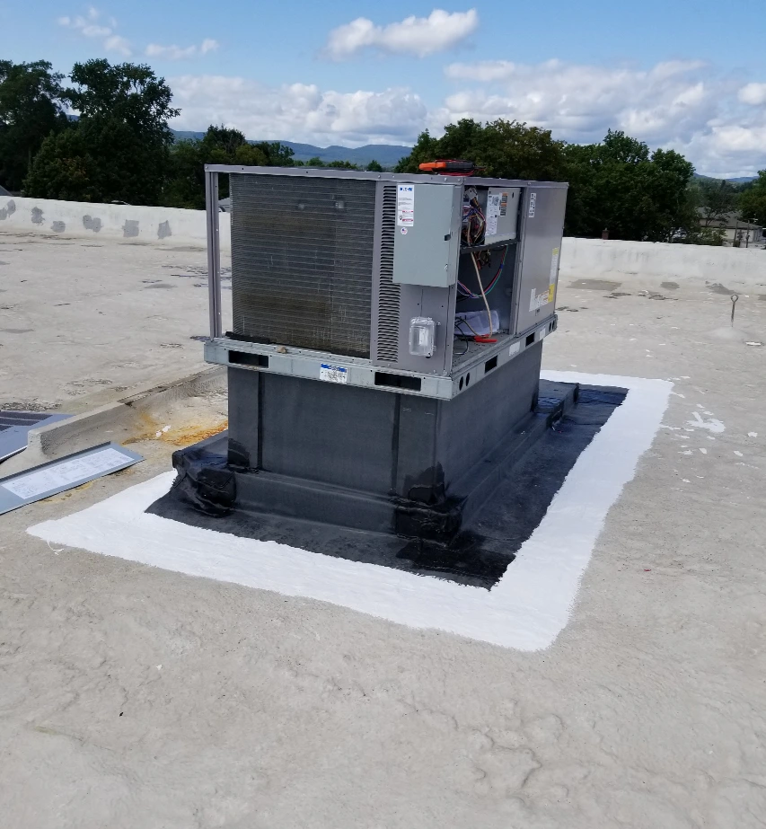 A rooftop view of a commercial flat roof with an air conditioner unit.