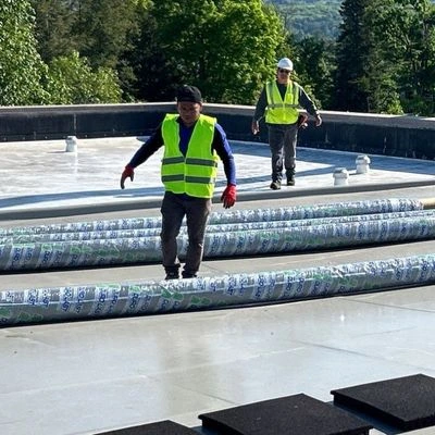 Roofing contractors in safety gear laying out rolled roofing membrane materials on a commercial flat roof surface in New York