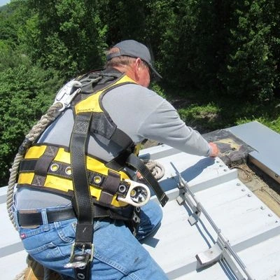 Professional roofer wearing full safety harness equipment while working on commercial roof installation in New York using specialized roofing tools
