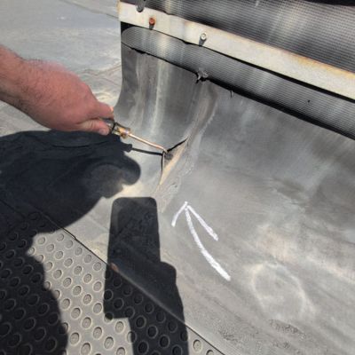 Roofer's hand and tool indicating a tear in an industrial roof membrane displaying the need for commercial roof maintenance