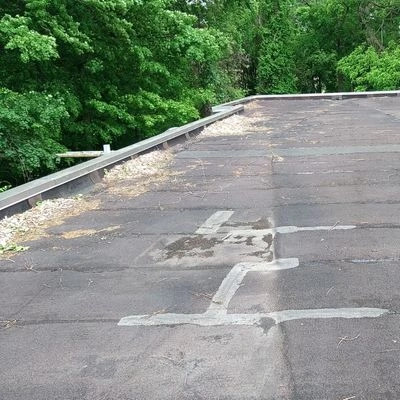 Aged flat roof with visible patchwork and debris buildup along the roof edge near the gutters.