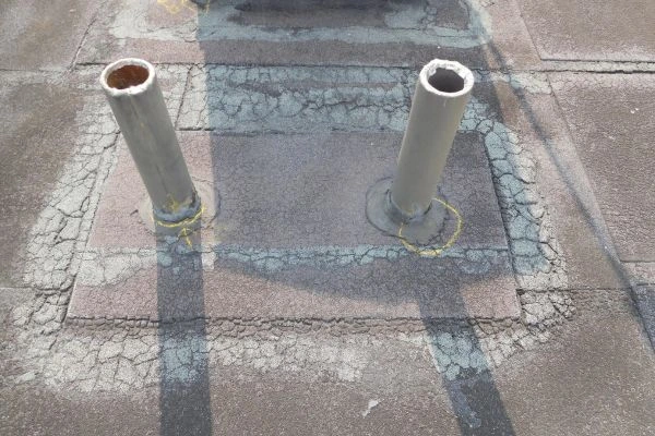 Close-up of cracked and deteriorated roofing material around vent pipes on a commercial flat roof.