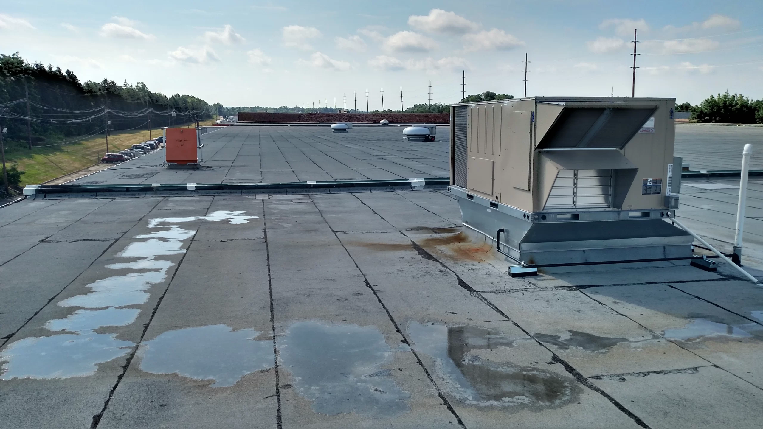 Flat commercial roof with standing water and an HVAC unit showing early signs of neglect and drainage issues.