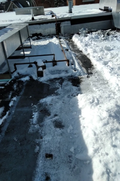 Close-up view of a cleared path around rooftop mechanical equipment and piping on a snowy commercial roof.