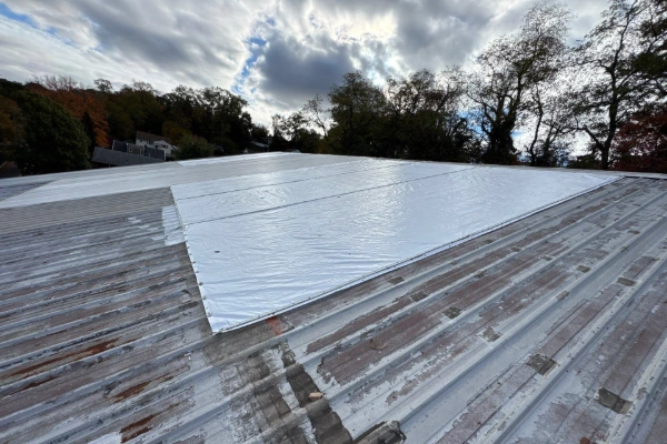 Heavy-duty tarp providing temporary emergency protection on damaged commercial metal roof