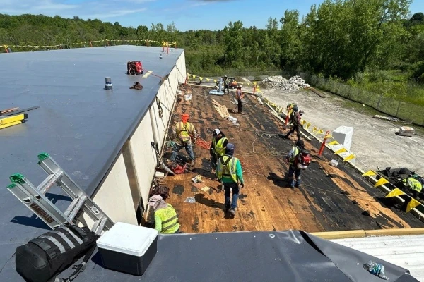 Roofing crew removing and replacing a flat roof membrane on a large commercial industrial facility