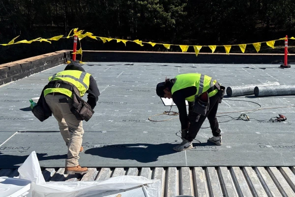 Two roofing technicians fastening a new flat roof membrane on a commercial building with safety barriers in place