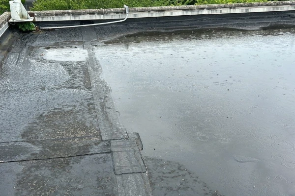 Standing water pooling across a flat commercial roof surface during rainfall, showing inadequate drainage.