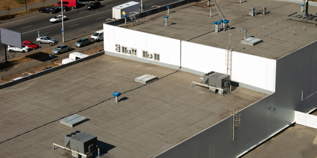 Commercial flat roof with HVAC units, vents, and roof access ladders on a low-slope building